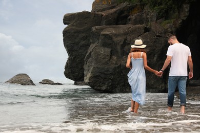 Photo of Young couple walking on beach near sea, back view. Space for text