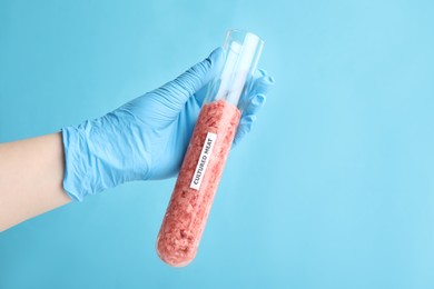 Scientist holding test tube with minced cultured meat on light blue background, closeup