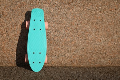 Light blue skateboard with pink wheels near wall outdoors. Space for text