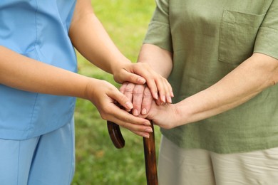 Photo of Elderly woman with walking cane and female caregiver outdoors, closeup