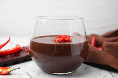 Photo of Glass of hot chocolate with chili pepper on white textured table