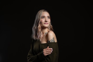 Photo of Beautiful woman with tattoos on body against black background
