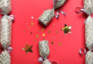 Open and closed Christmas crackers with shiny confetti on red background, flat lay