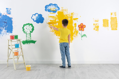 Little child painting wall with roller brush indoors