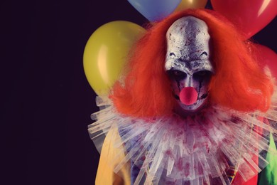 Photo of Terrifying clown with air balloons on black background, space for text. Halloween party costume