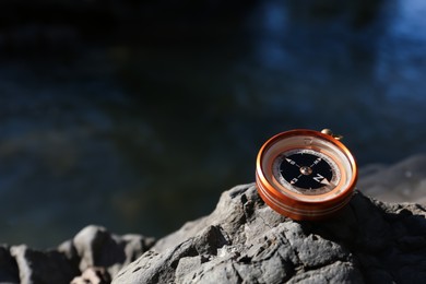 Compass on rock near river outdoors. Space for text
