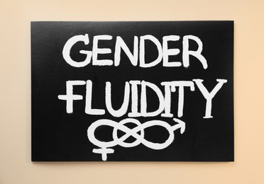 Photo of Black card with text Gender Fluidity, male and female symbols on beige background, top view