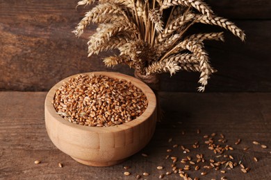 Wheat grains in bowl and spikes on wooden table