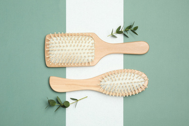 Wooden hair brushes and green twigs on color background, flat lay