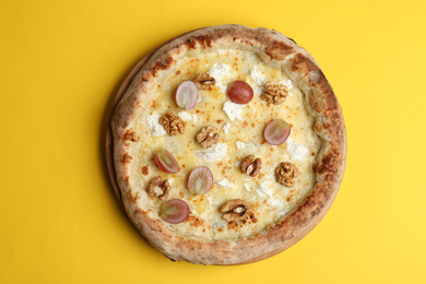Photo of Delicious cheese pizza with grapes and walnuts on yellow background, top view