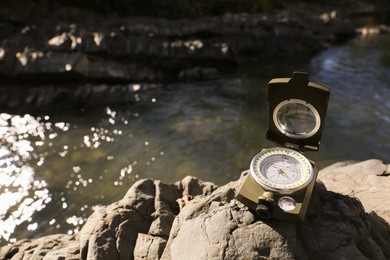 Compass on rock near river. Space for text