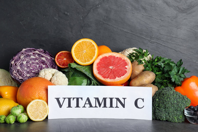 Different products and card with phrase VITAMIN C on black table