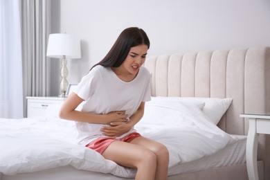Young woman suffering from stomach ache in bedroom