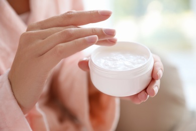 Woman with jar of moisturizing cream on blurred background, closeup