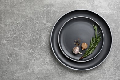 New dark plates with rosemary, garlic and peppercorns on light grey table, top view. Space for text