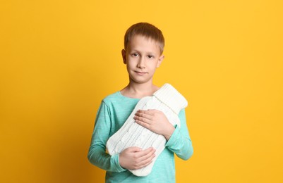 Ill boy with hot water bottle suffering from cold on yellow background