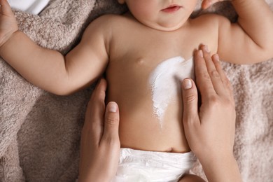 Mother applying moisturizing cream onto her little baby's skin on towel, closeup