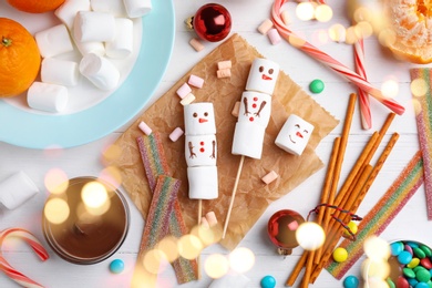 Flat lay composition with funny snowmen made of marshmallows on white wooden table. Bokeh effect
