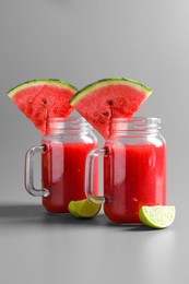 Tasty summer watermelon drink with lime in glass mason jars on grey background