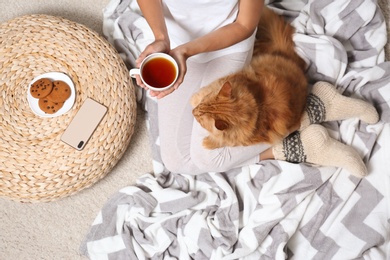 Woman with cute red cat and tea on blanket, top view