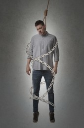 Depressed man with rope noose on neck and metal chains around him against grey background