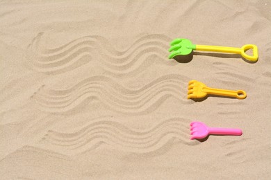 Plastic rakes on sand, space for text. Beach toys