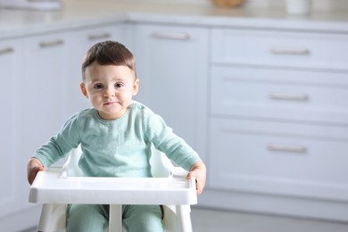 Cute little baby sitting in high chair at kitchen. Space for text