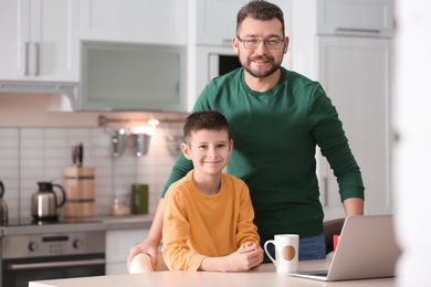 Little boy and his dad using laptop in kitchen