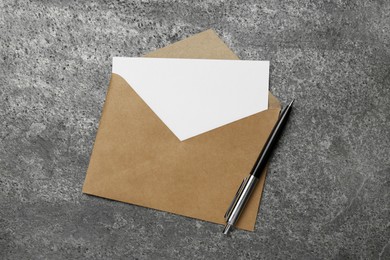 Envelope with blank paper card and pen on grey table, top view