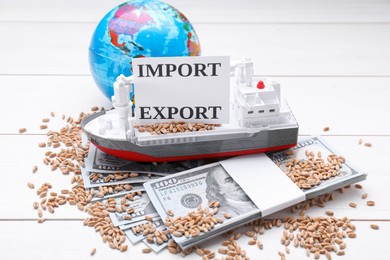 Card with words Import and Export near globe, wheat grains, money and toy cargo vessel on white wooden table