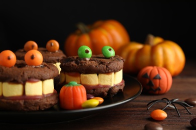 Delicious desserts decorated as monsters on wooden table, closeup. Halloween treat