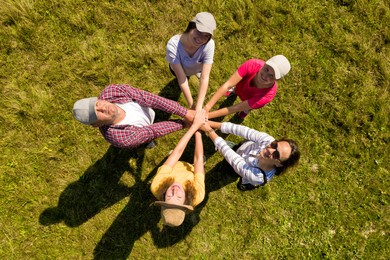Top aerial view of happy people holding hands together in circle on green grass. Drone photography