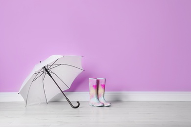 Beautiful open umbrella and gumboots on floor near color wall with space for design