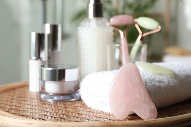 Photo of Rose quartz gua sha tool, natural face rollers and toiletries on wicker table indoors. Space for text