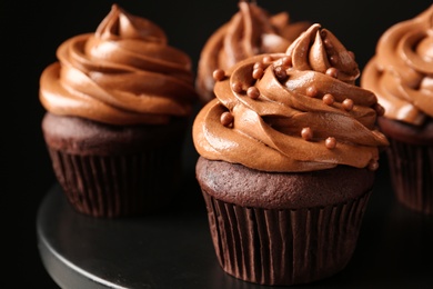 Delicious chocolate cupcakes with cream and beads on black table, closeup