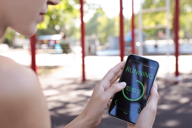 Young woman using fitness app on smartphone outdoors, closeup