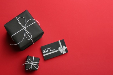 Gift card and presents on red background, flat lay. Space for text