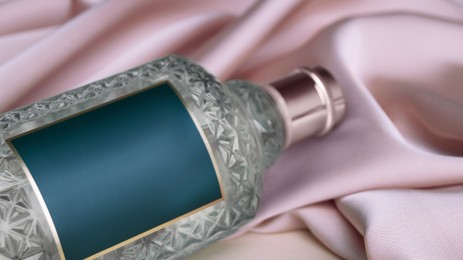 Photo of Bottle of luxurious perfume on beige silk, closeup