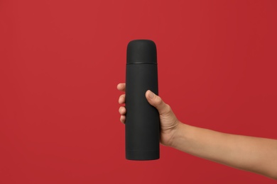 Woman holding modern black thermos on red background, closeup