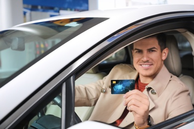 Man sitting in car and showing credit card at gas station, focus on hand