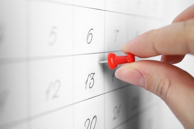 Woman pinning Friday 13th on calendar, closeup. Bad luck superstition