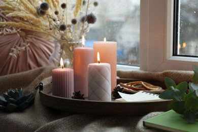 Tray with burning wax candles and decor on window sill indoors
