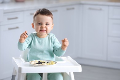 Cute little baby eating healthy food in high chair at home. Space for text