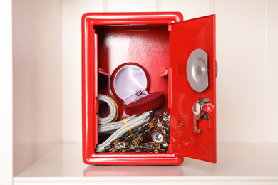Open red steel safe with money and jewelry on shelf