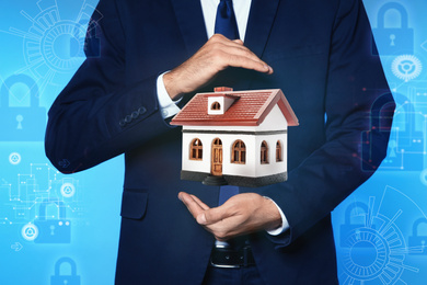 Home security concept. Man holding house on light blue background, closeup