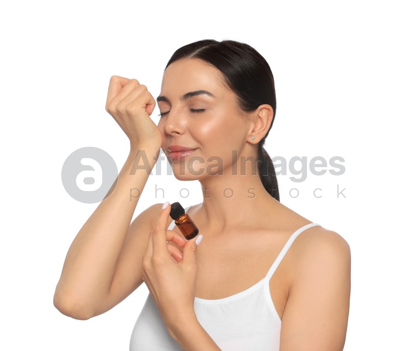 Young woman smelling essential oil on wrist against white background