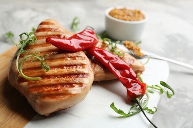 Tasty grilled chicken fillets with chili peppers and arugula on board, closeup
