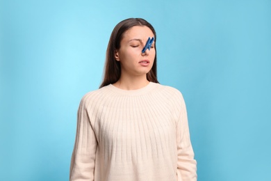 Photo of Young woman with clothespin on light blue background. Runny nose concept
