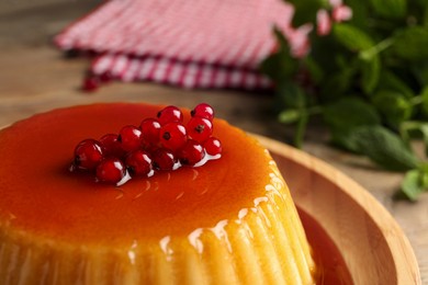 Photo of Delicious pudding with caramel and redcurrants on wooden table, closeup