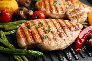 Tasty grilled chicken fillets with vegetables on frying pan, closeup